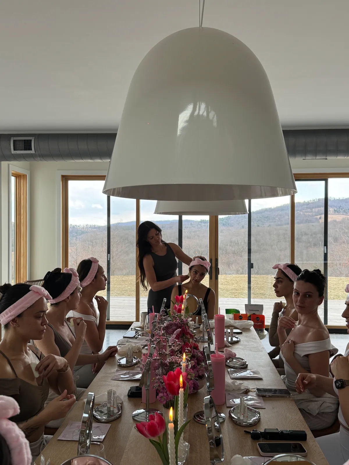 Guests in pink spa headbands seated around a mirrored table while the instructor demonstrates, mountain view beyond, at a Mind & Body Retreats beauty workshop