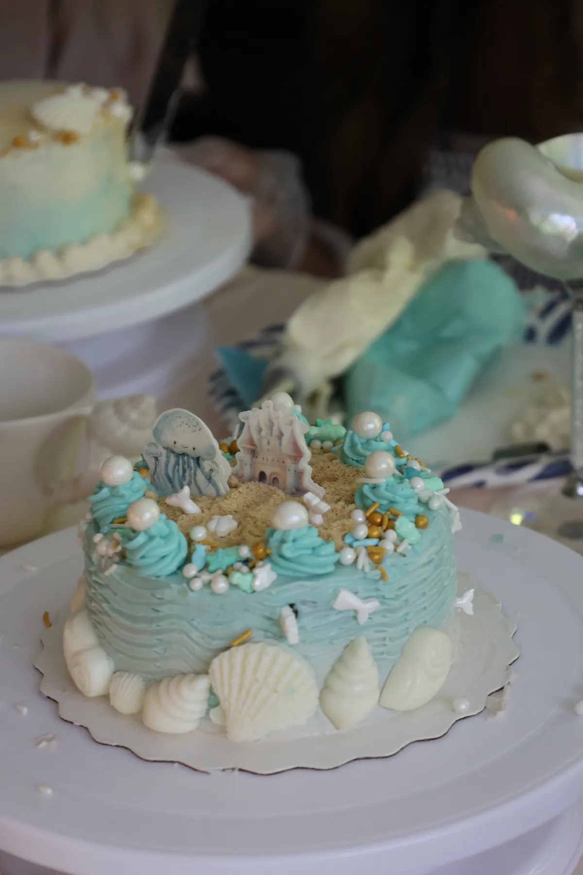 Finished ocean-themed cake iced in pale blue buttercream with white chocolate shells and pearls at a Mind & Body Retreats cake decorating workshop