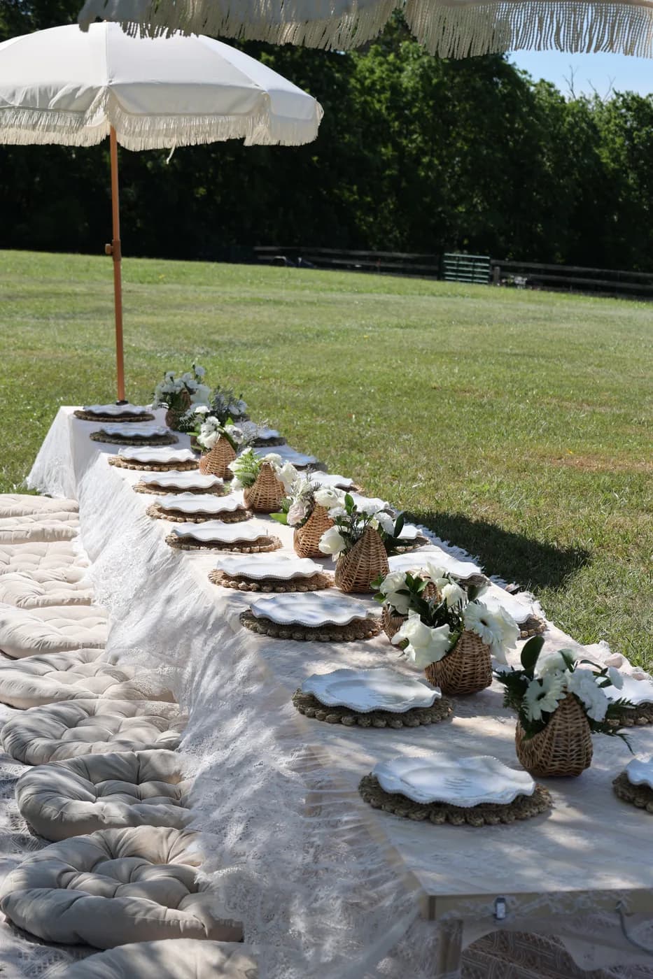 Lace-covered picnic table with wicker baskets and fringe umbrellas beside a saddled horse at a Mind & Body Retreats farm event