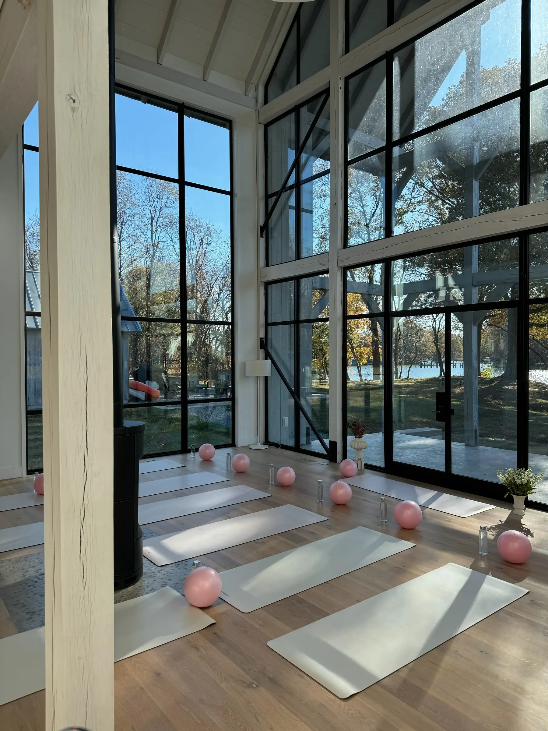 Pilates mats and pink toning balls laid out in a sunlit lakeside studio with floor-to-ceiling windows, set for a Mind & Body Retreats session